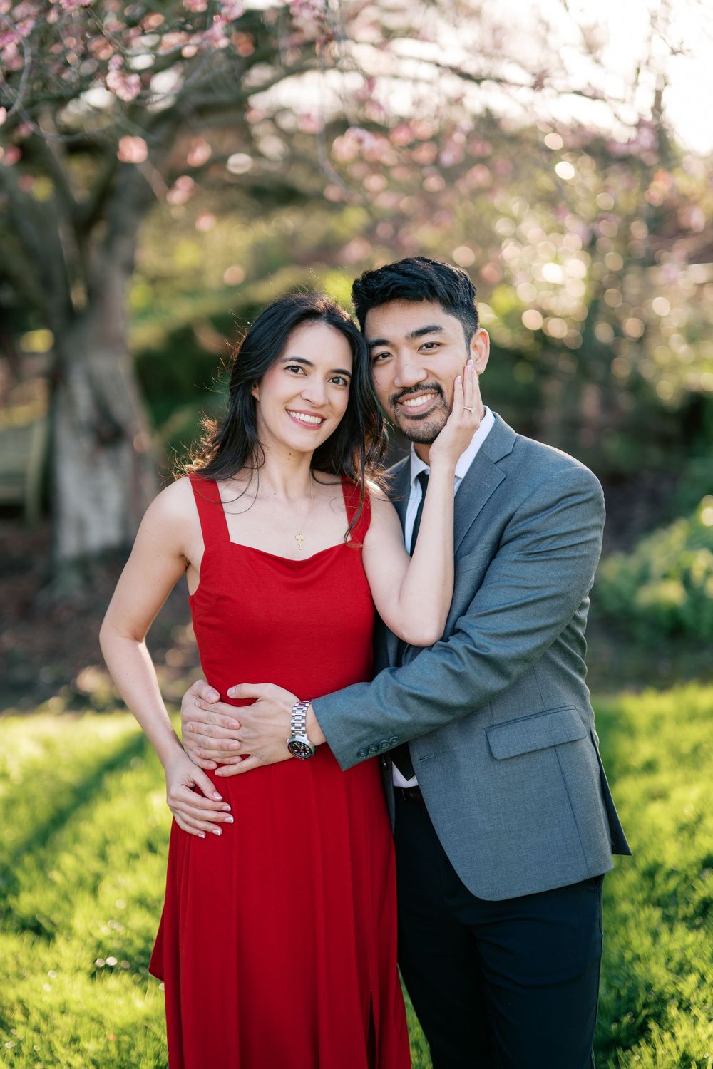 A romantic couple embraces in a garden with blooming cherry blossoms and soft sunlight.