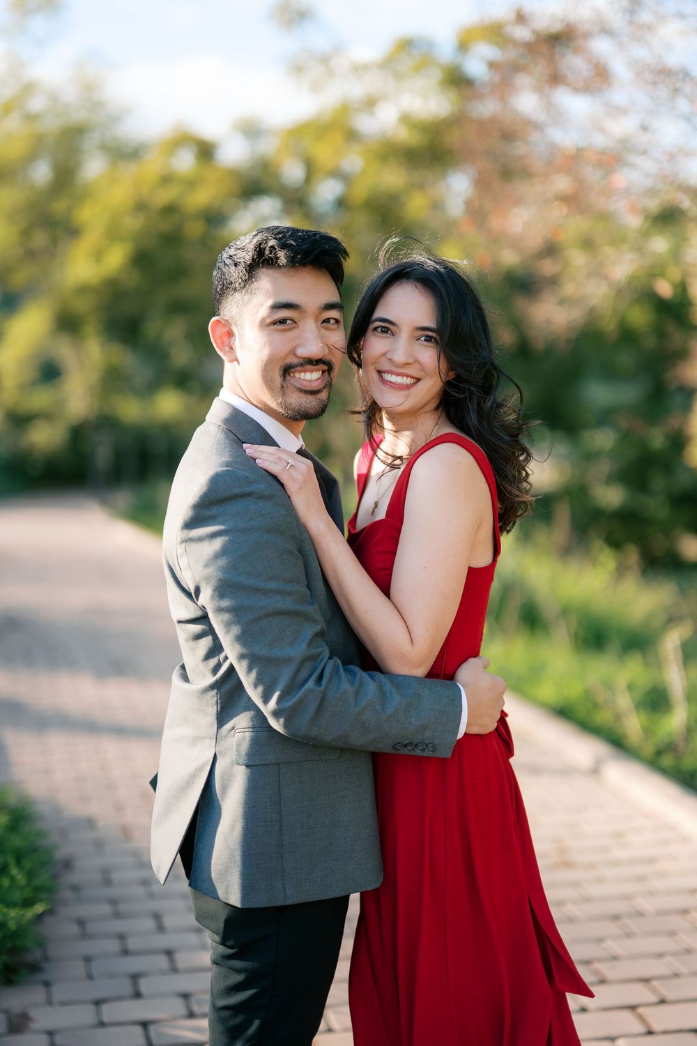 A couple in formal attire shares romantic moments on a brick path with autumn foliage in the background.