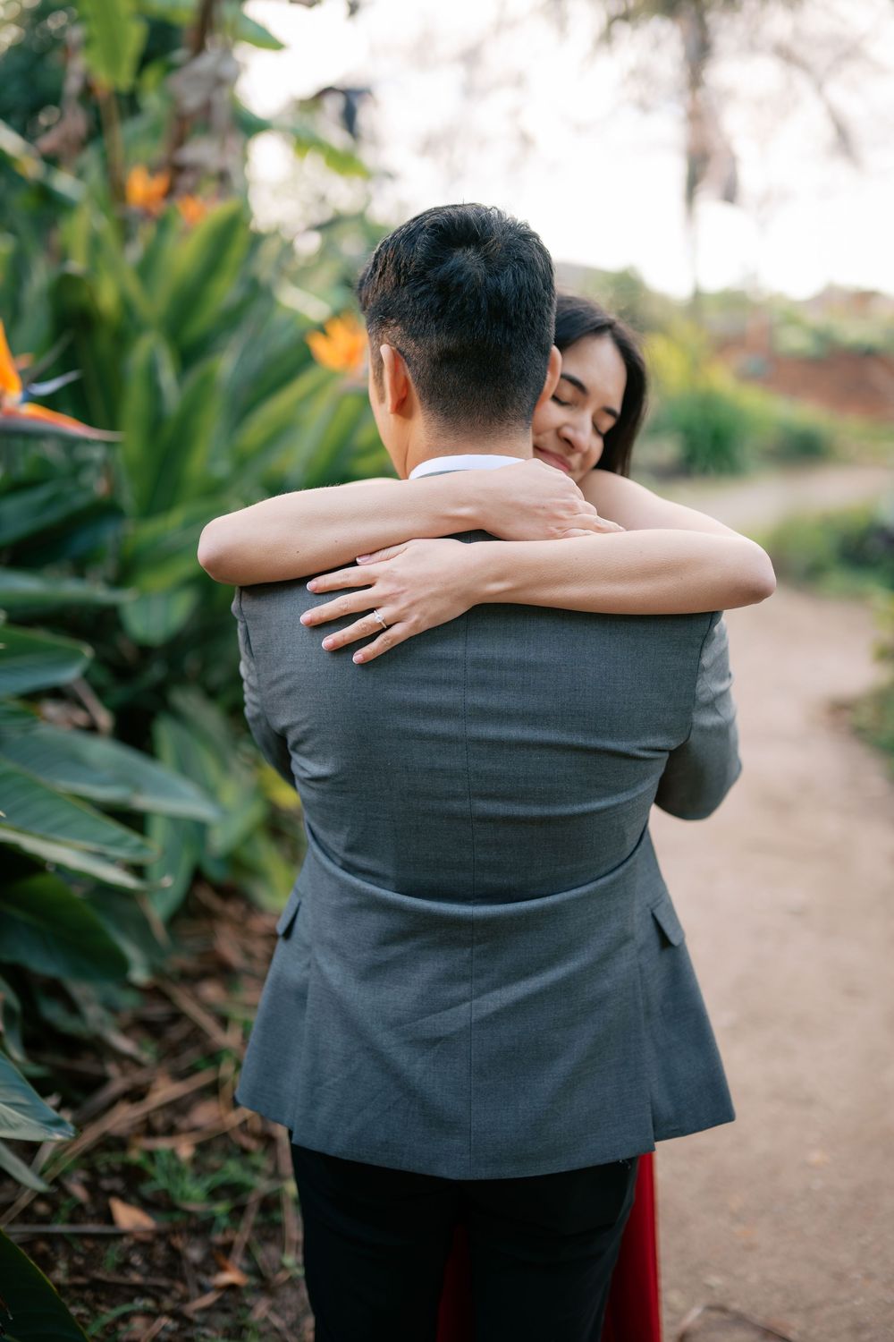A tender embrace between two people on a garden path surrounded by tropical plants and foliage.