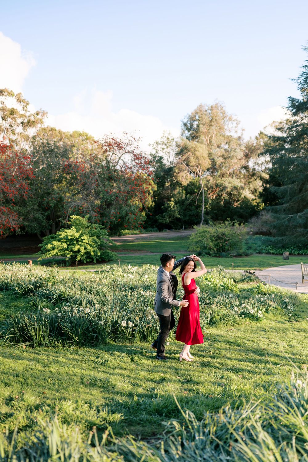 A couple dances together on a grassy hillside in a garden setting during golden hour.