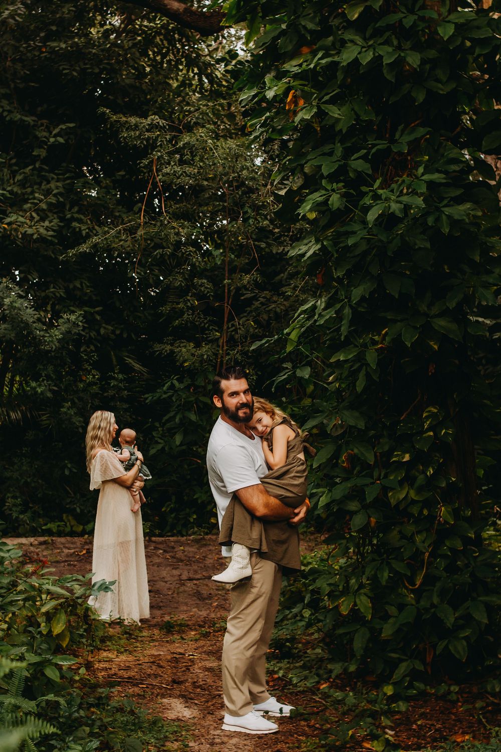 A couple shares an intimate moment while dancing together in a lush garden setting with green foliage surroundings.