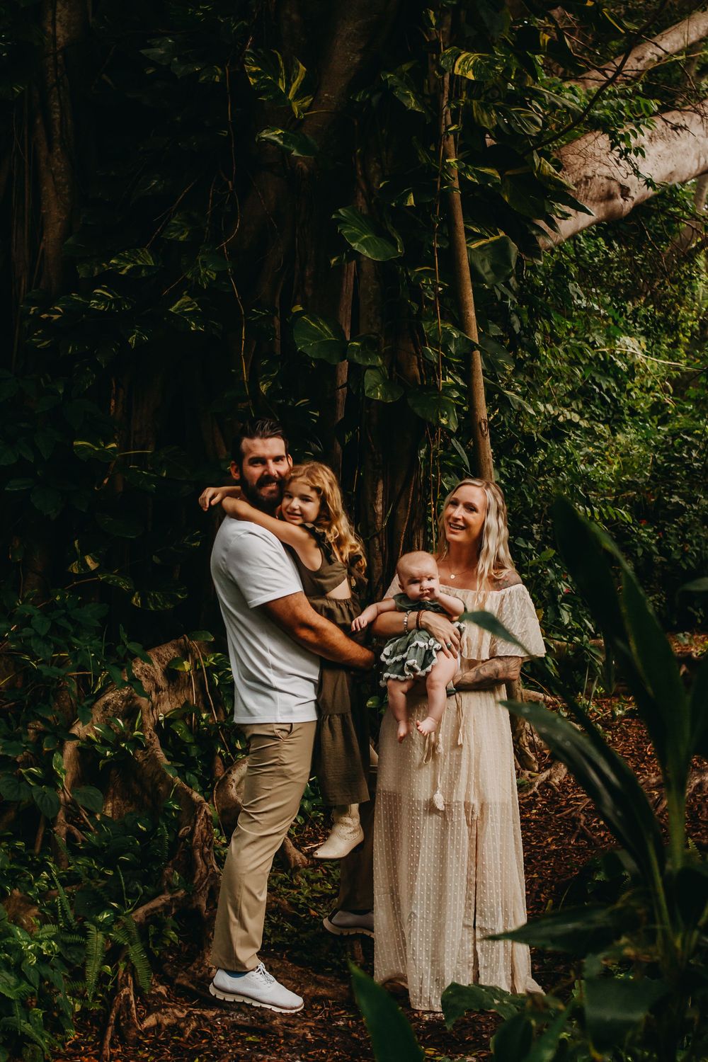 A family shares a tender moment together in a lush forest setting during golden hour.