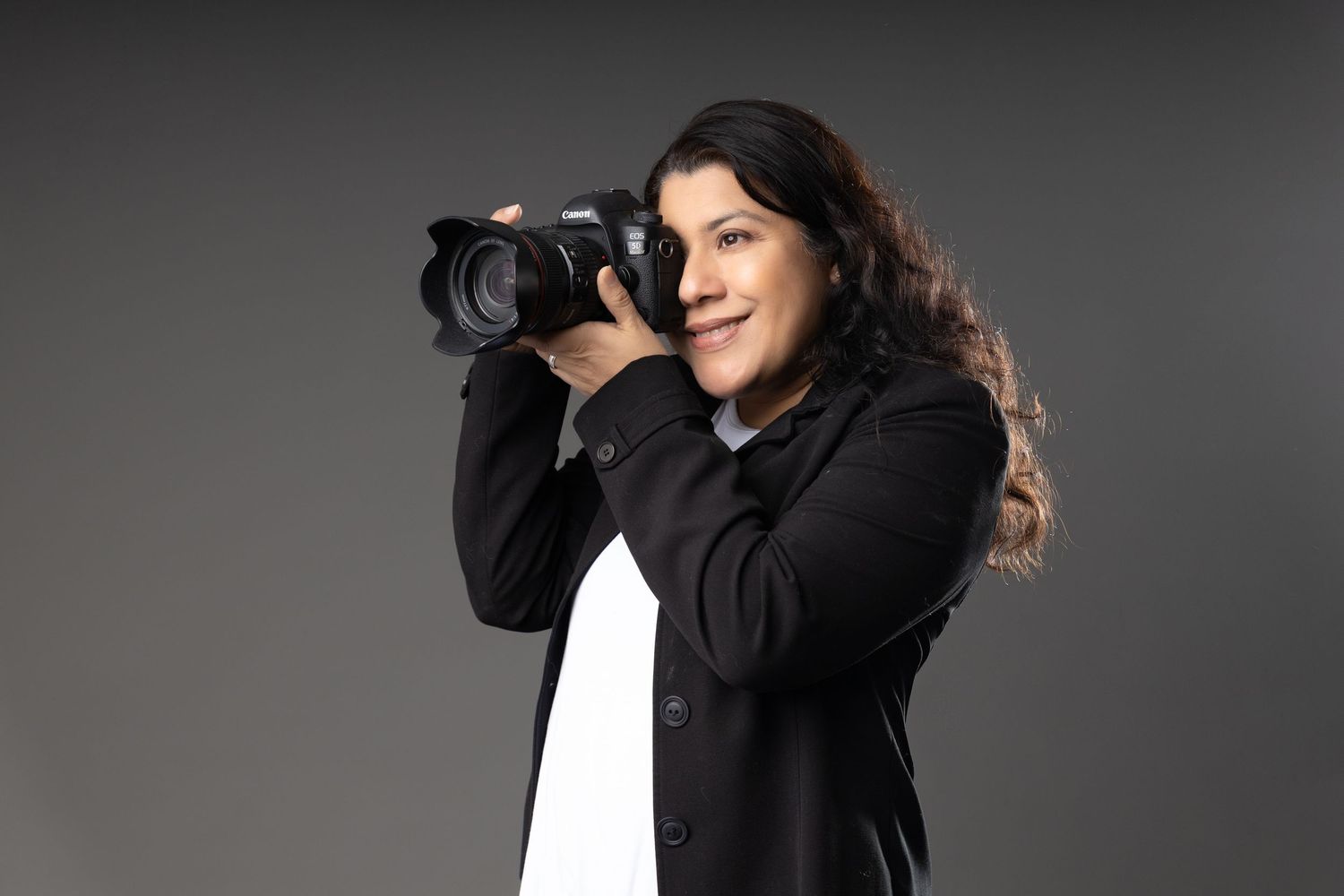 Professional photographer wearing black clothing adjusts camera settings while shooting in a studio setting.