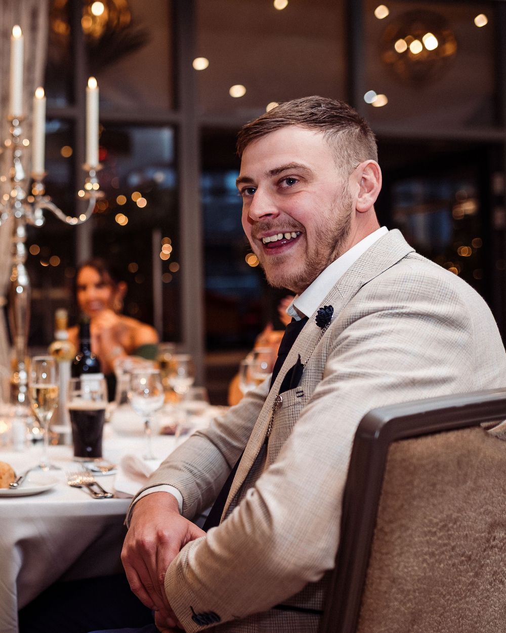 A person in a light colored hoodie sits at an elegant dining table with glowing candlelight and ambient lighting.
