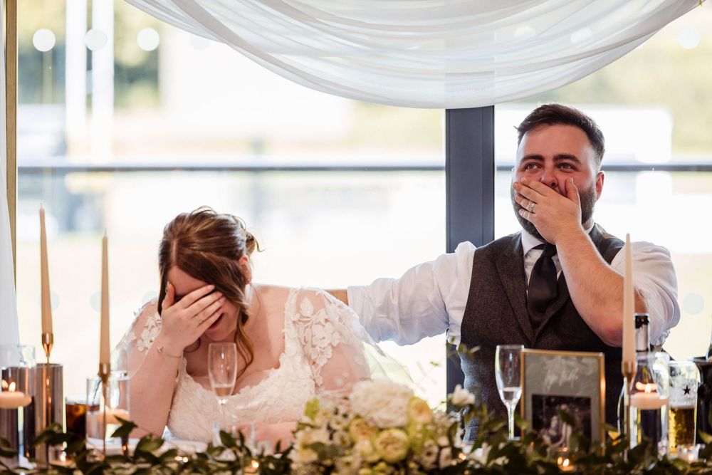 Wedding guests react emotionally during heartfelt reception speeches at an elegant venue with white draping decor.