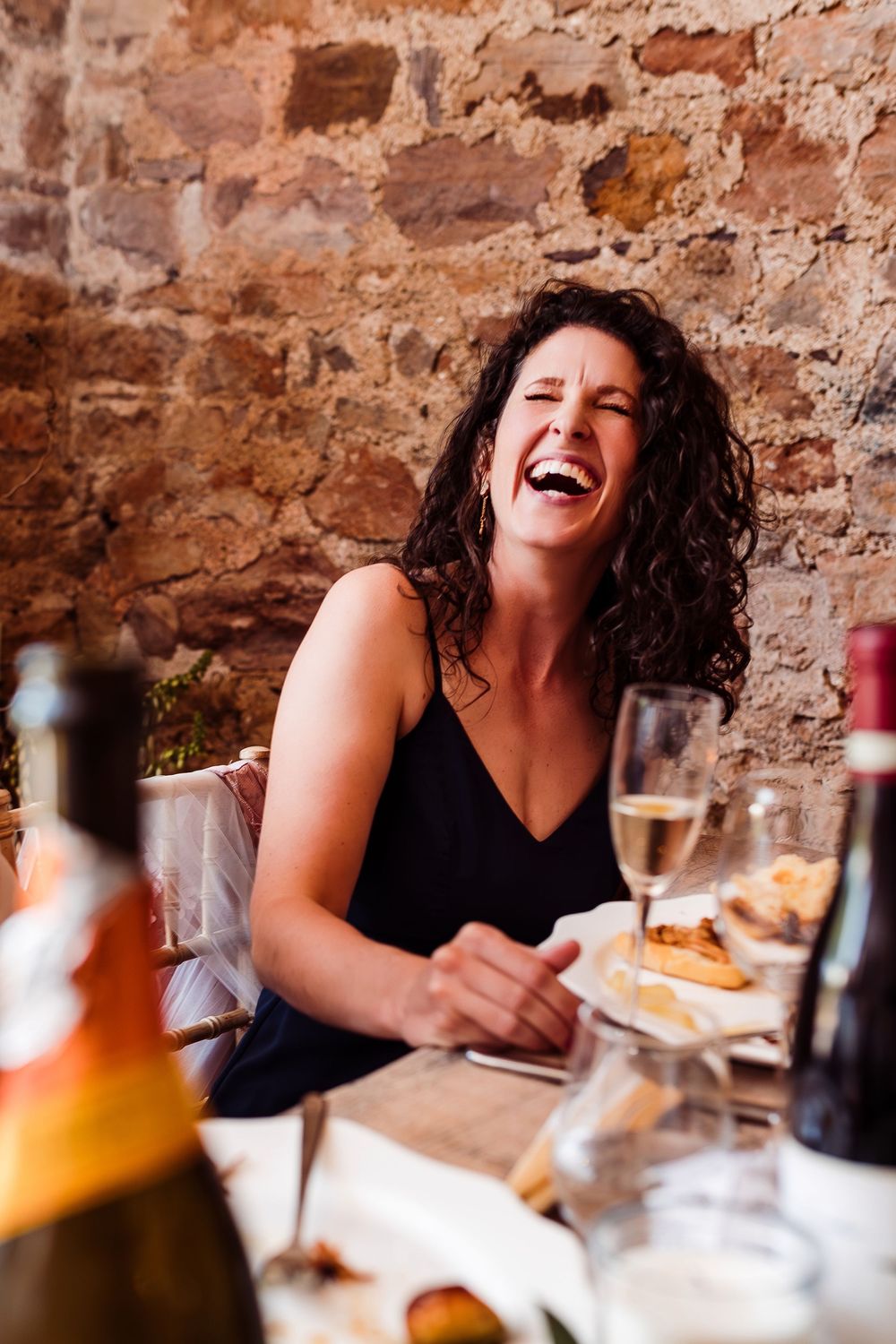 A joyful moment captured during dinner at a rustic restaurant with wine bottles and food on the table.