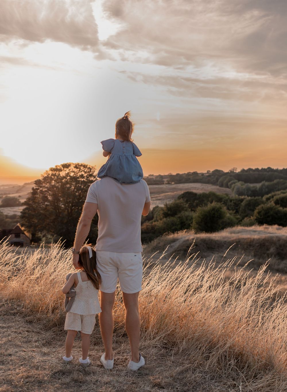 Father with two young children watching a golden sunset over rolling countryside fields.