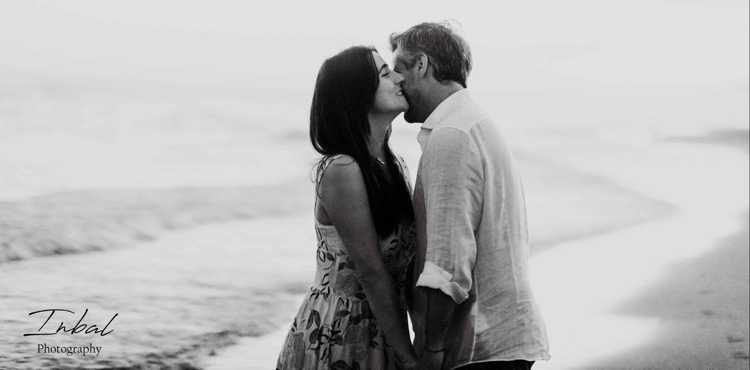 An Old grain black-and-white photo of a couple kissing on the cheek and holding hands on the beach.