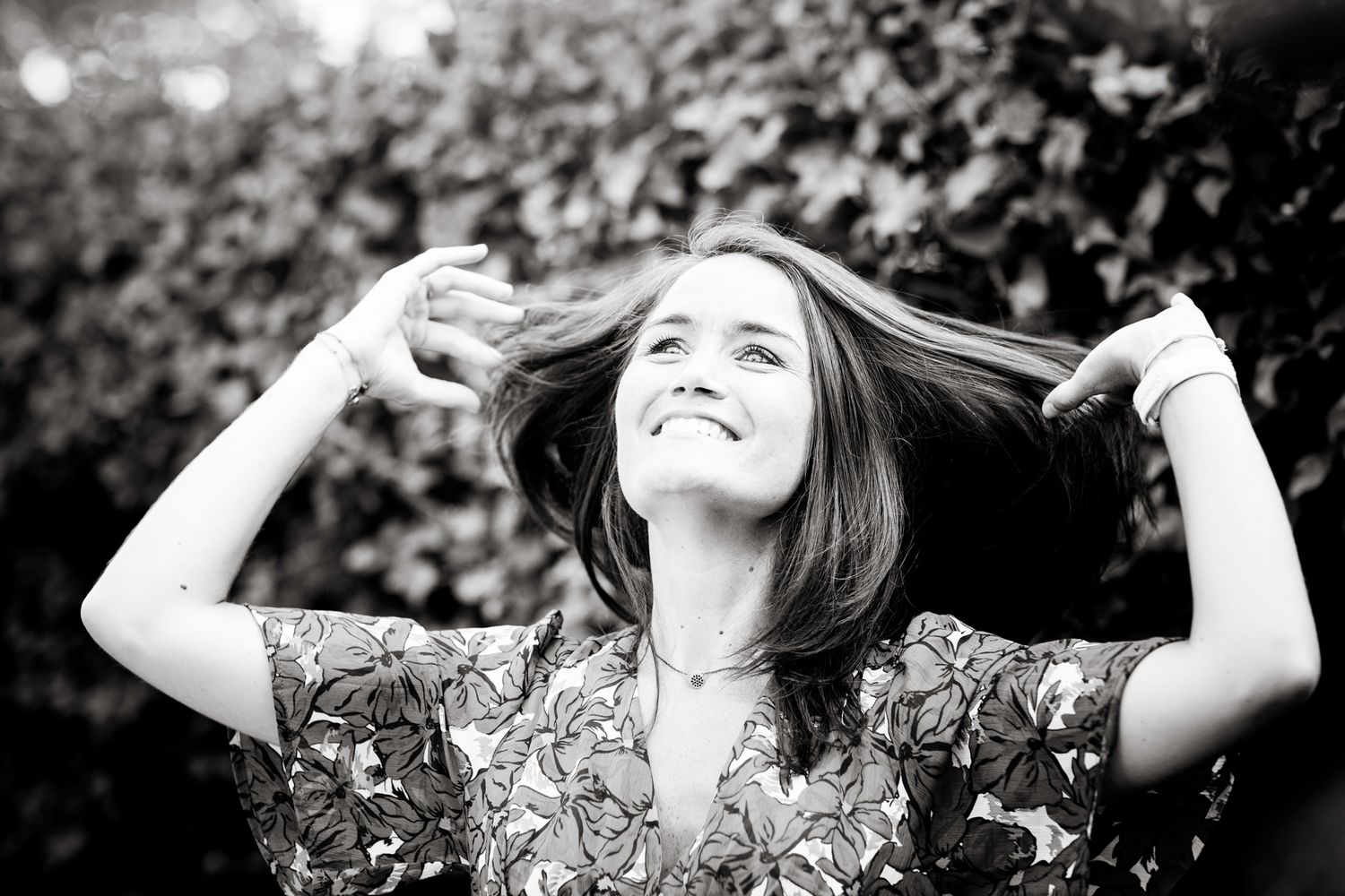 A black-and-white image of a woman touching her hair with her two hands looking up at a garden in a private villa in Marbella.