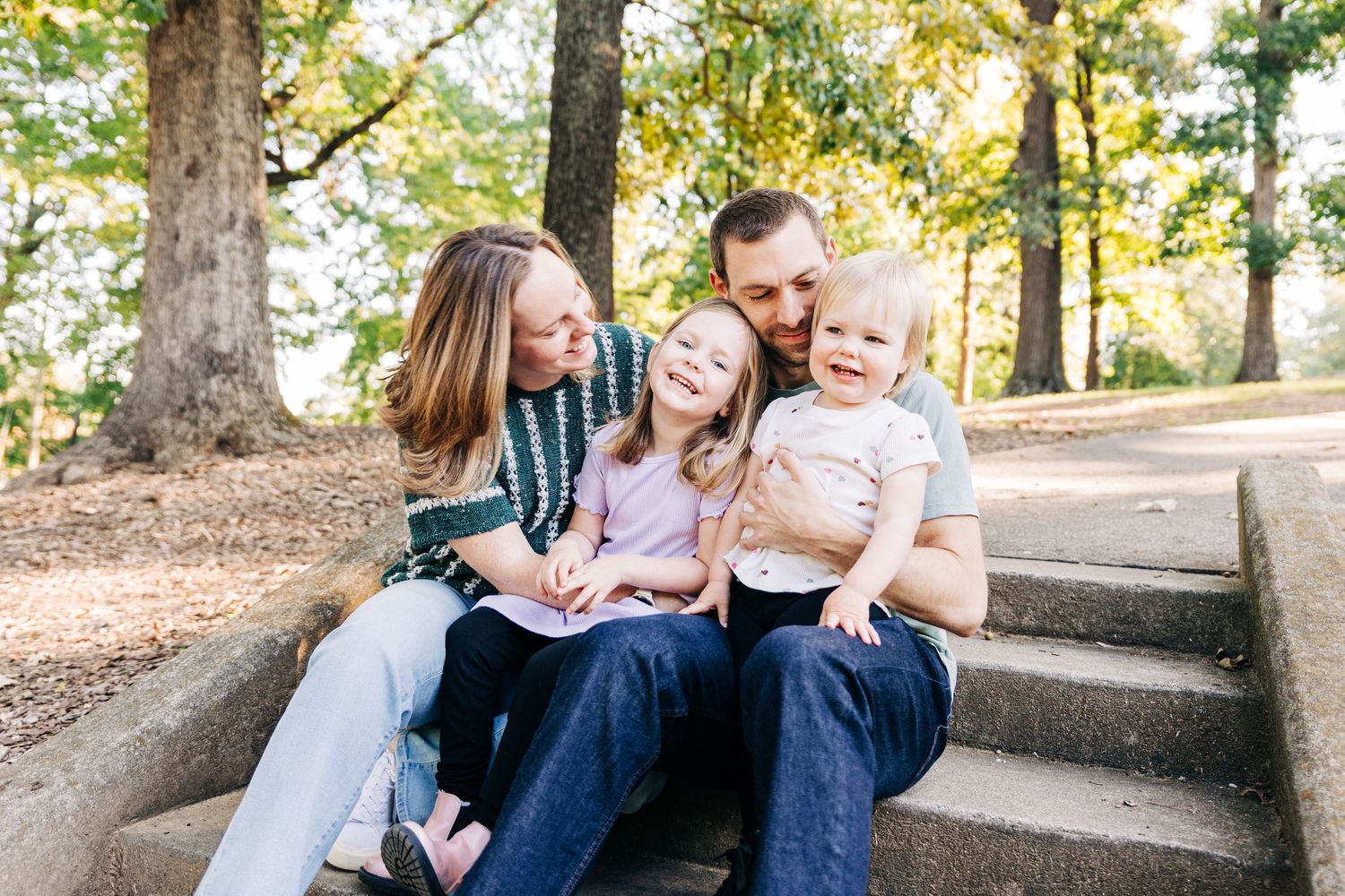 A family sits together on a stone wall in a park during an autumn photoshoot session.