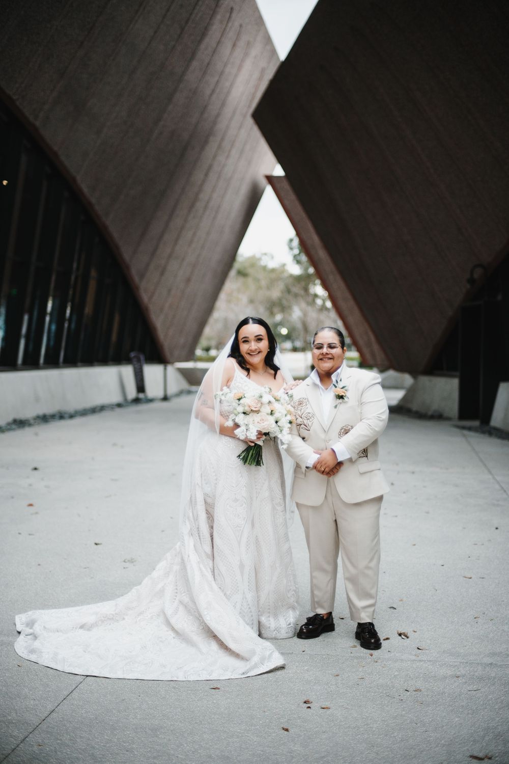 A wedding couple poses in front of a modern architectural structure with angular walls and geometric design.