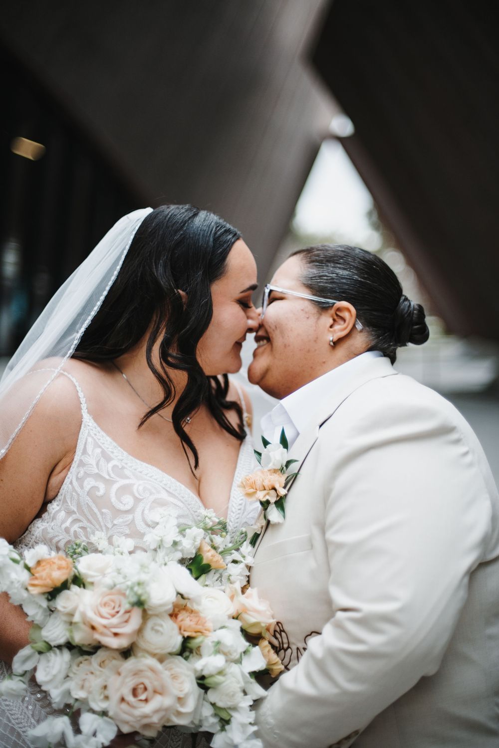 Romantic wedding couple shares intimate kisses while holding a peach and white rose bouquet.