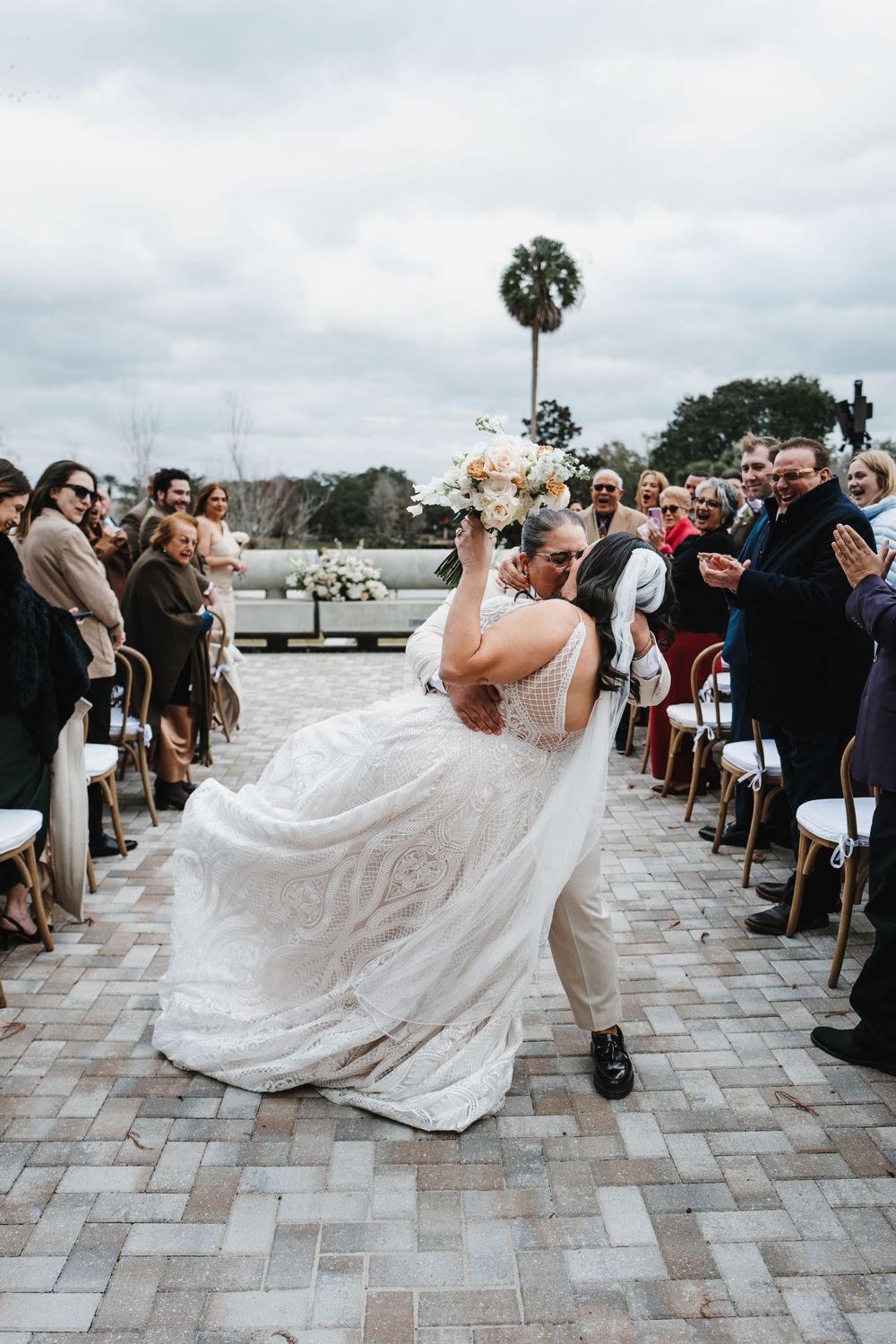 A wedding celebration on a stone patio as a person in a flowing white dress spins joyfully among seated guests.