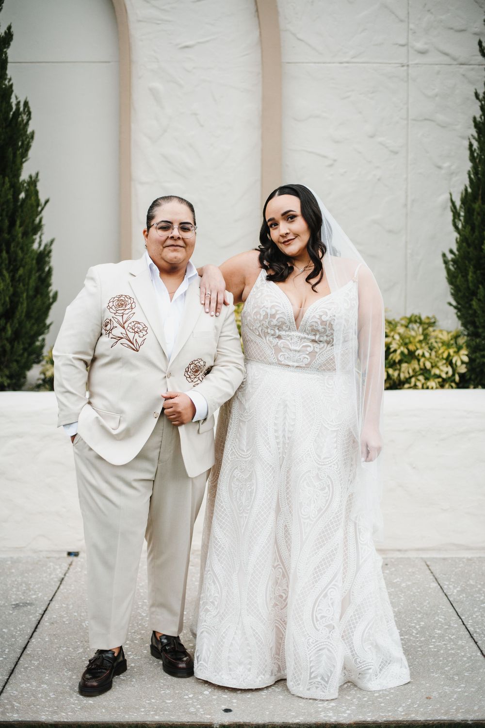 A couple in matching white outfits poses together in a series of wedding photos against a light-colored wall.