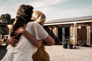A couple embraces tenderly in golden sunlight against a rustic building backdrop.