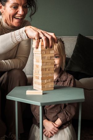 A person plays Jenga on a turquoise table, carefully removing blocks from the wooden tower as it leans precariously.