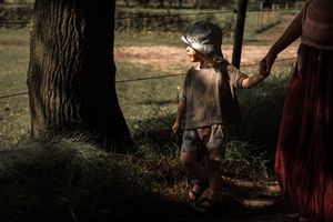 People in vintage clothing gather outdoors for a historical reenactment event in a wooded setting.