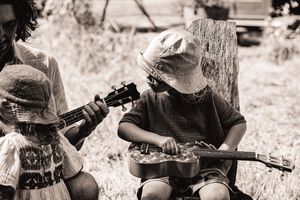 Musicians play acoustic instruments together in a casual outdoor jam session in black and white.