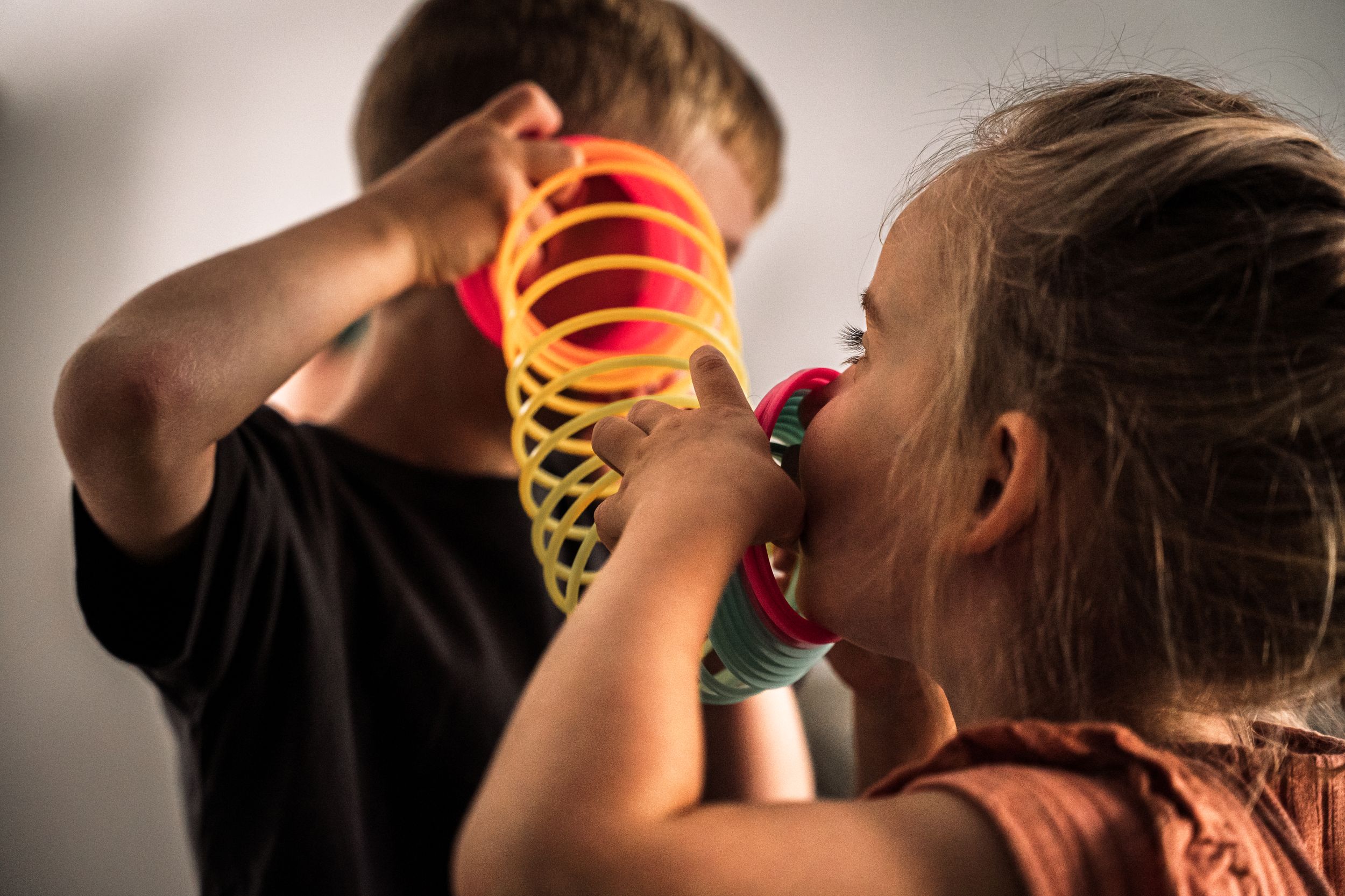 Two children playing with a colorful spiral slinky toy in warm lighting.