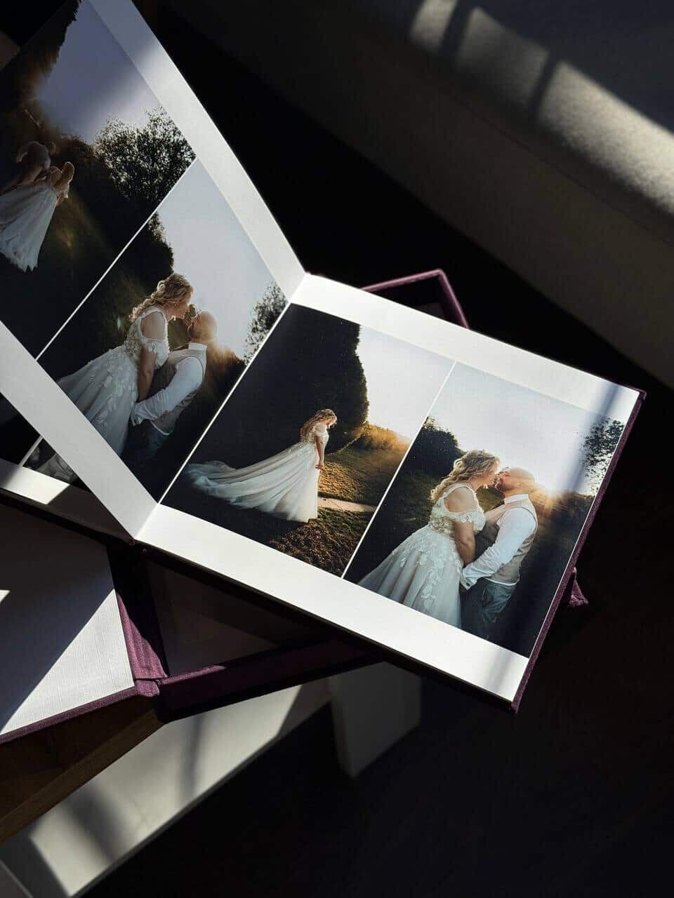 A wedding photo album lying open on a surface with sunlight casting shadows across elegant bridal portraits.