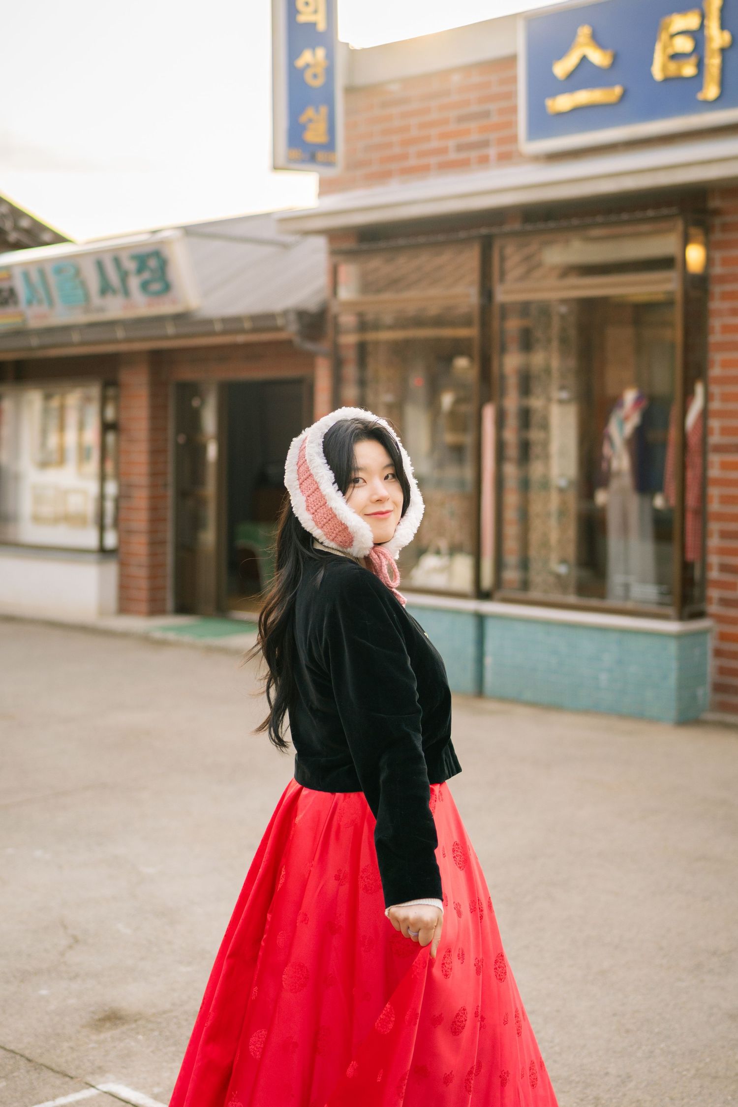 A person in a flowing red skirt twirls playfully on a brick-lined street with storefronts in the background.