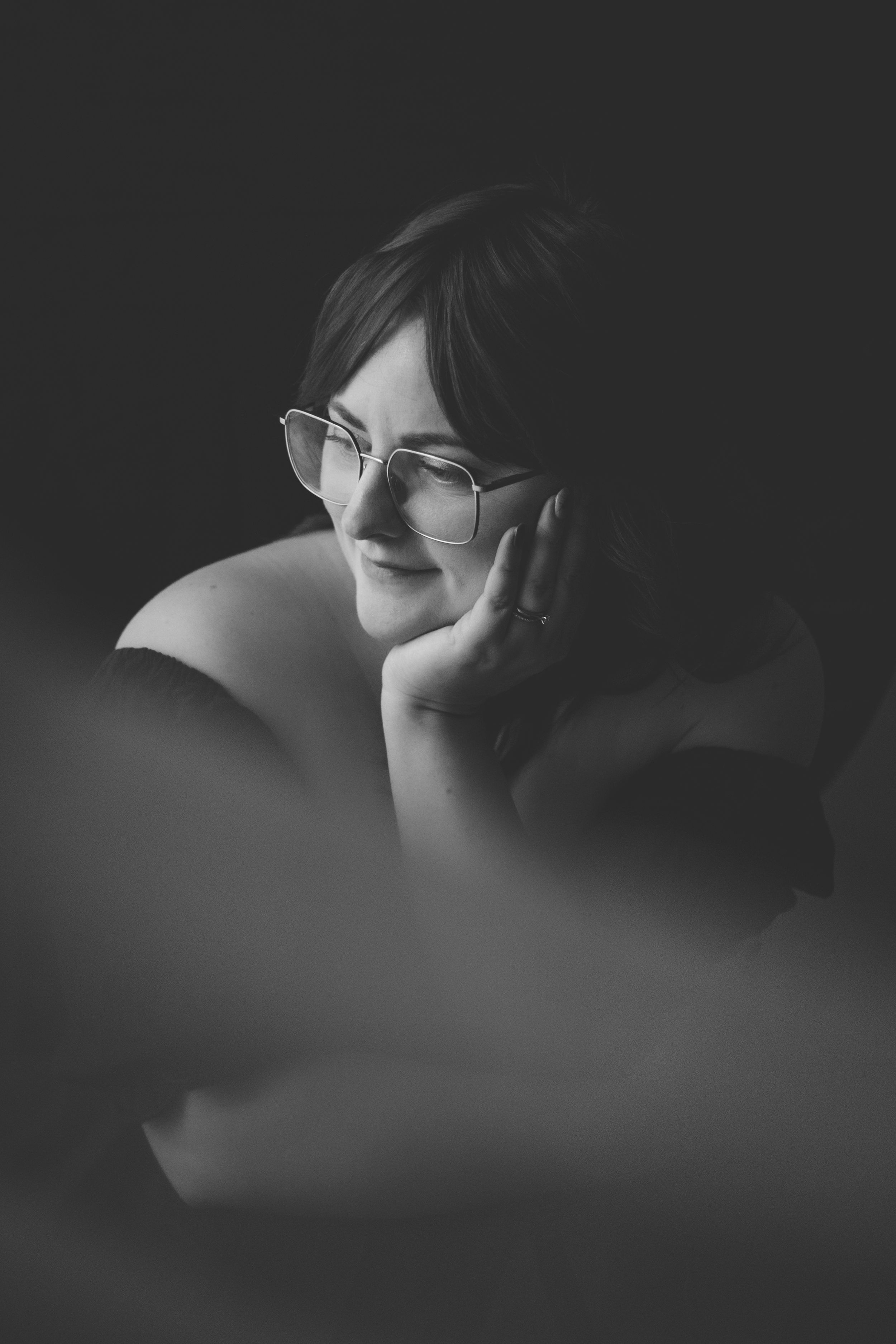 Professional photographer wearing a blazer and white top holds a camera with leather strap by window light.