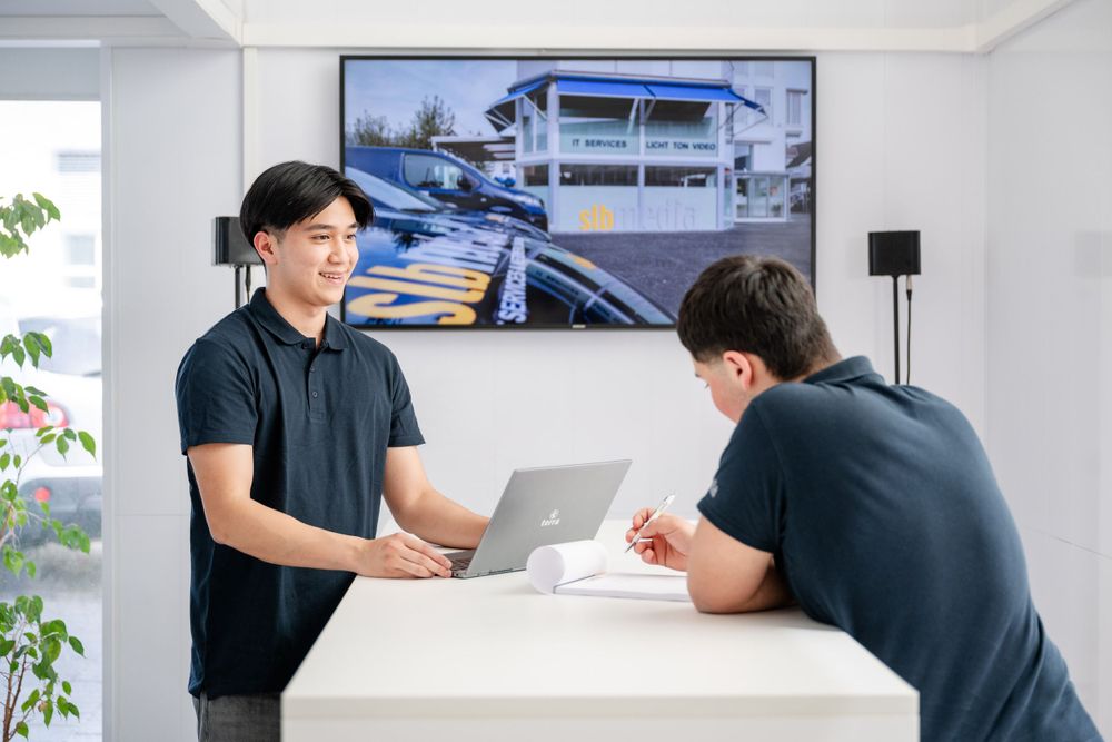 Team members reviewing documents at a white counter with a large display screen showing architecture.