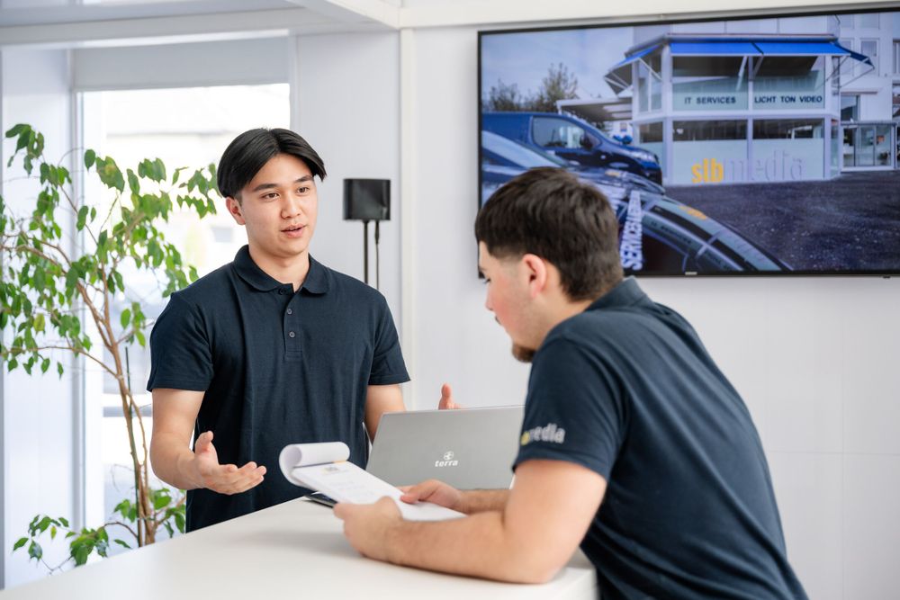 Staff members discussing paperwork at a modern office counter with display screen.