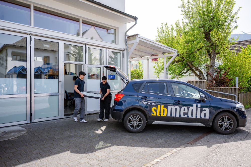 SB Media company car parked outside an office building entrance with people loading equipment.