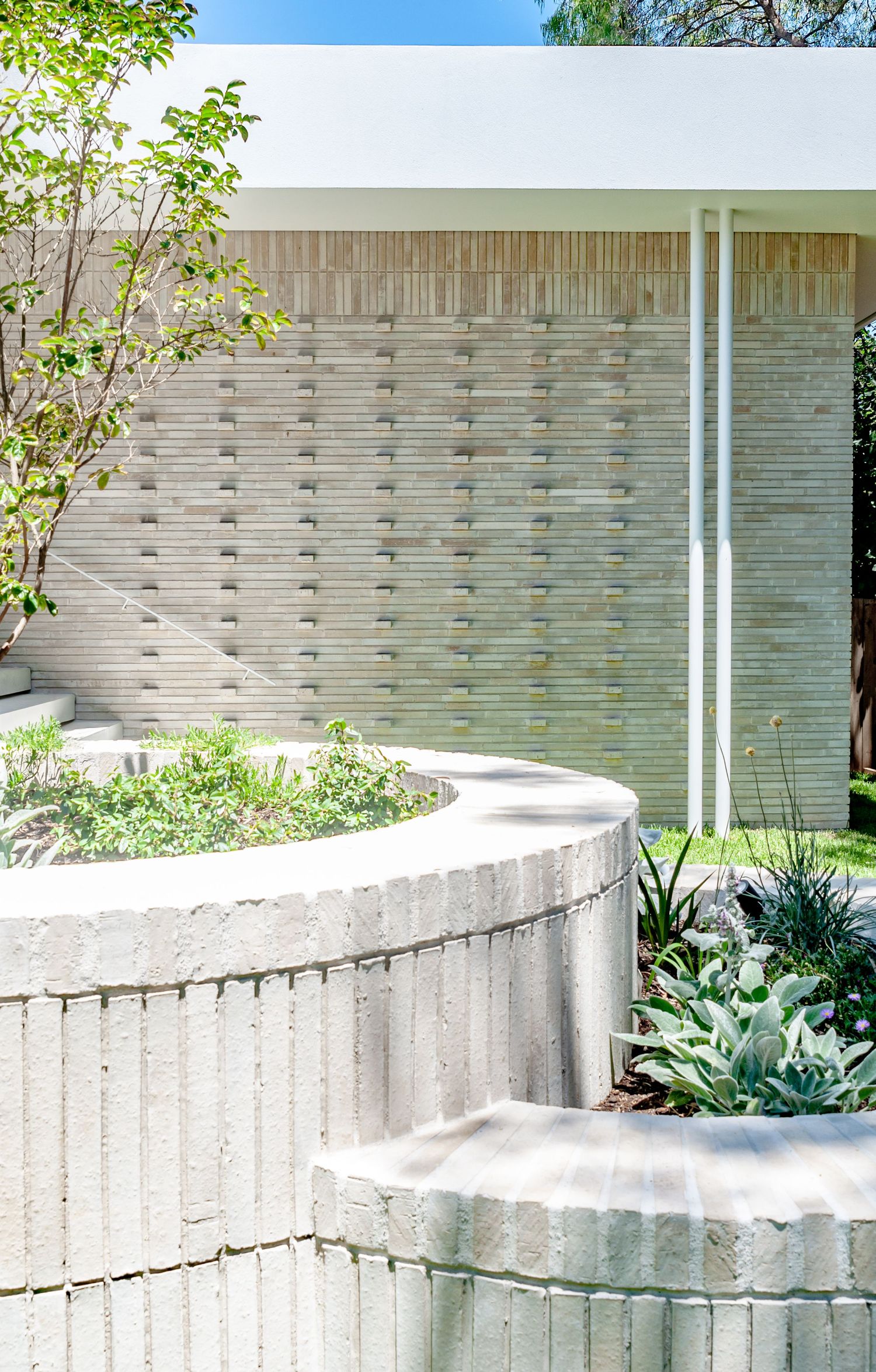 Detail shot of curved concrete planter with desert plants against geometric patterned wall.