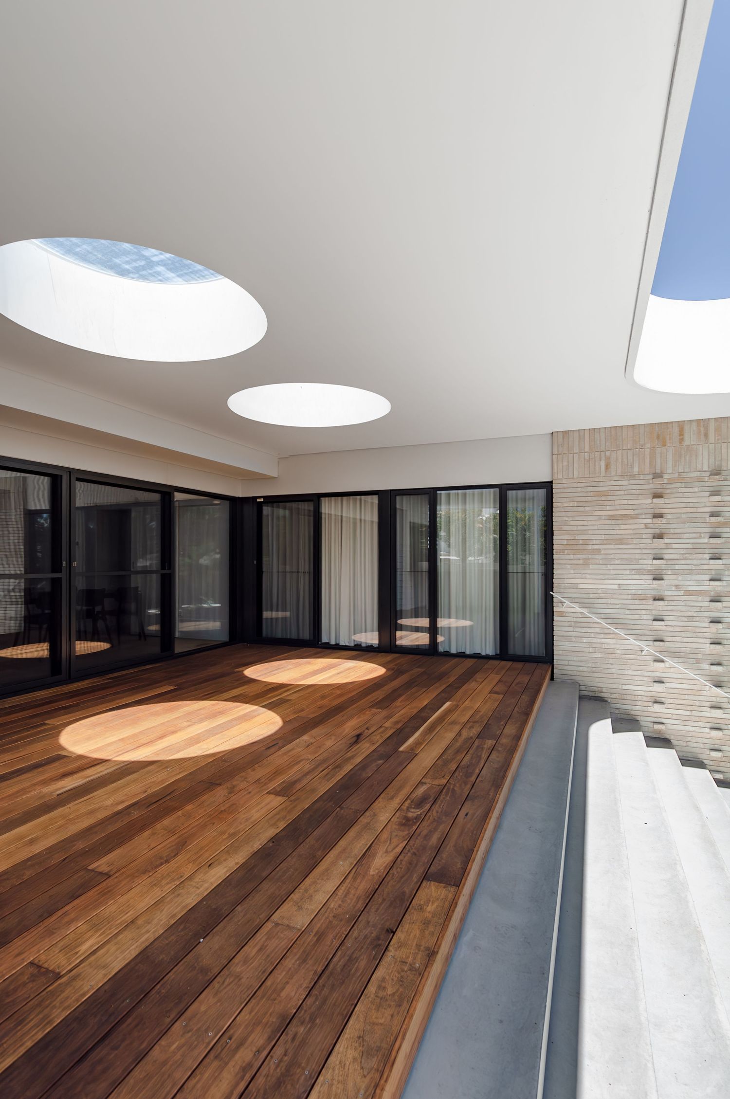 Interior view of modern space with wooden floors, glass walls, and circular skylights casting natural light.