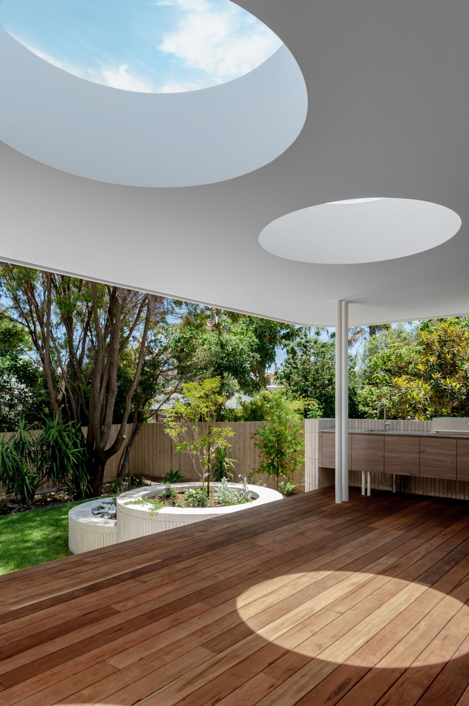 Modern outdoor deck with circular skylights casting sunlight patterns and a curved planter feature.