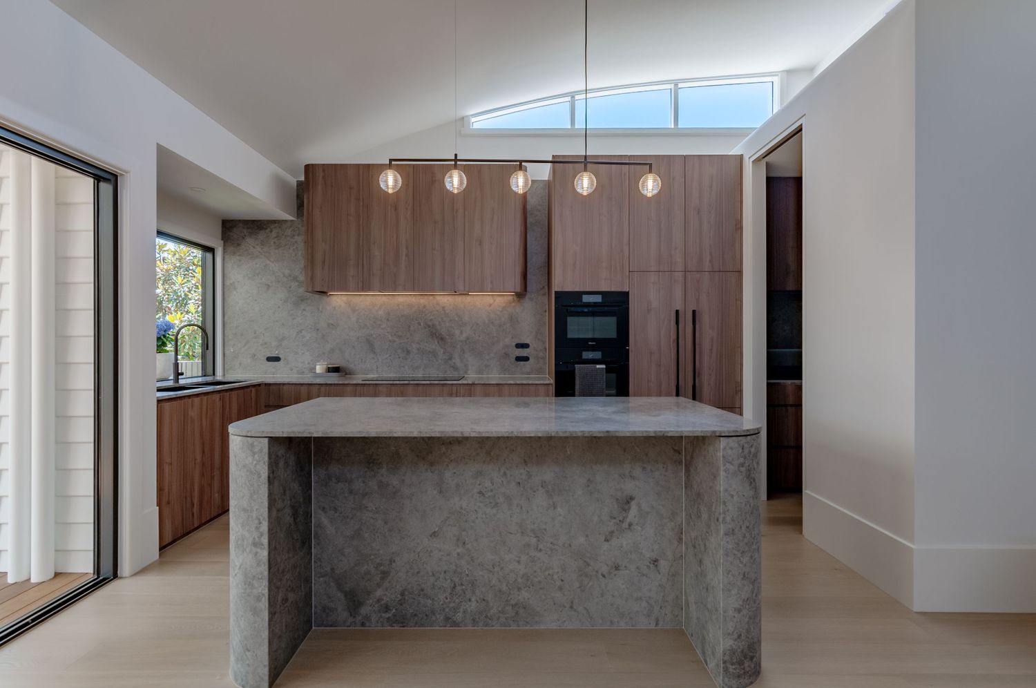 Contemporary kitchen with concrete waterfall island, wood cabinets, and natural light from skylight.