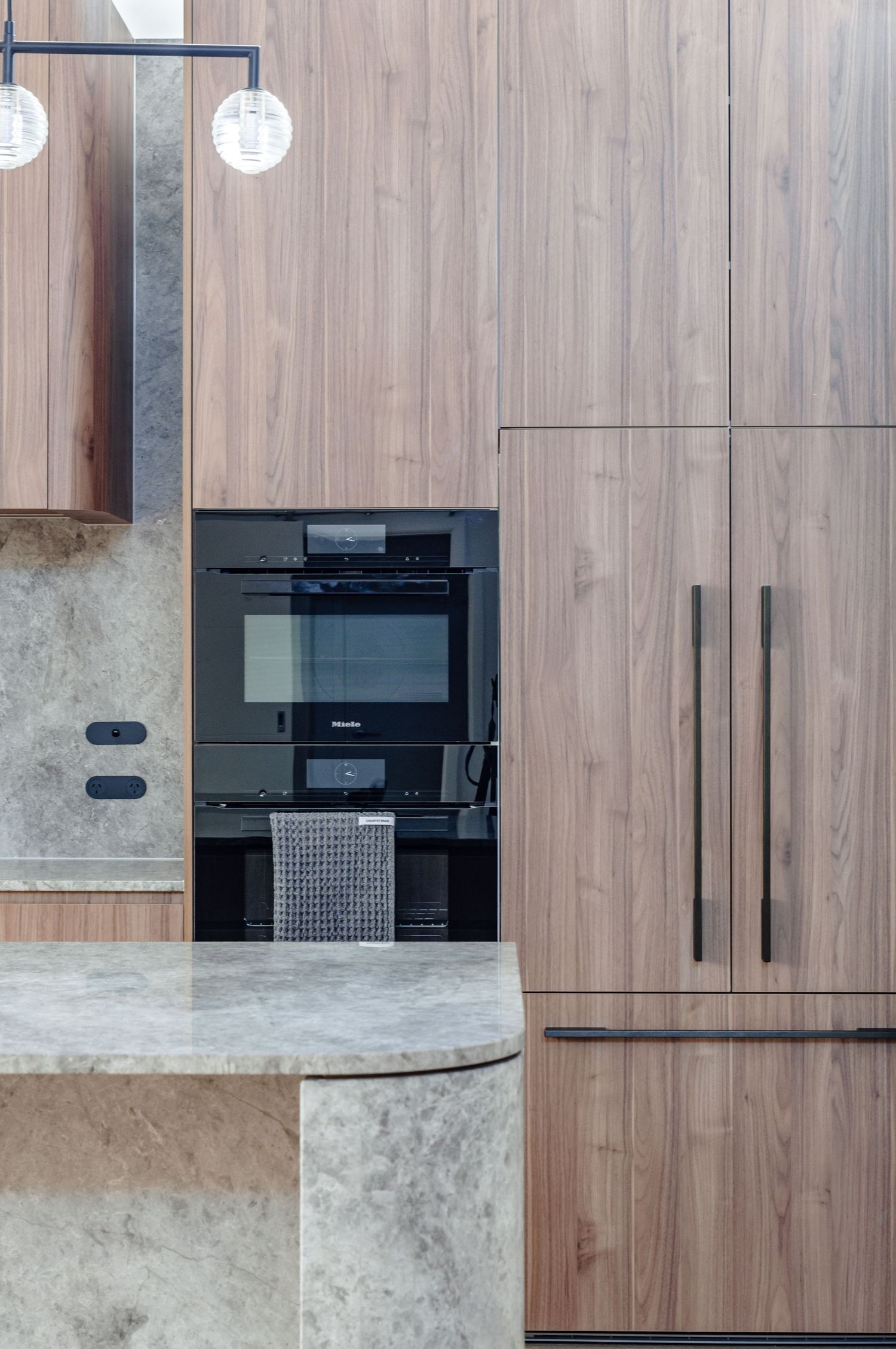 Modern kitchen detail showing built-in appliances and wood cabinetry with pendant lighting.