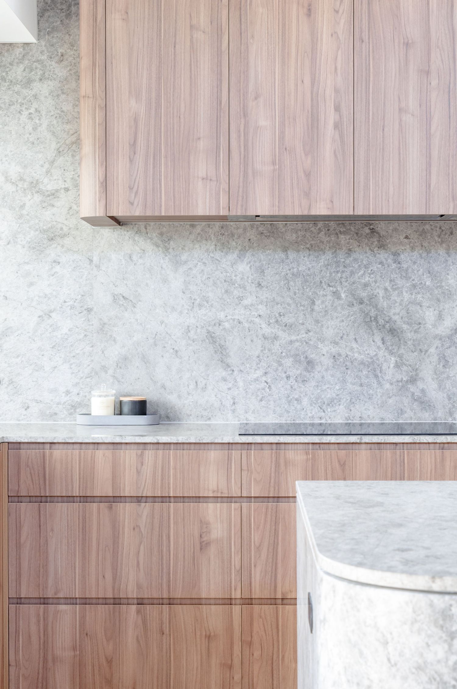 Minimalist kitchen design with wood cabinets and gray marble countertops and backsplash.