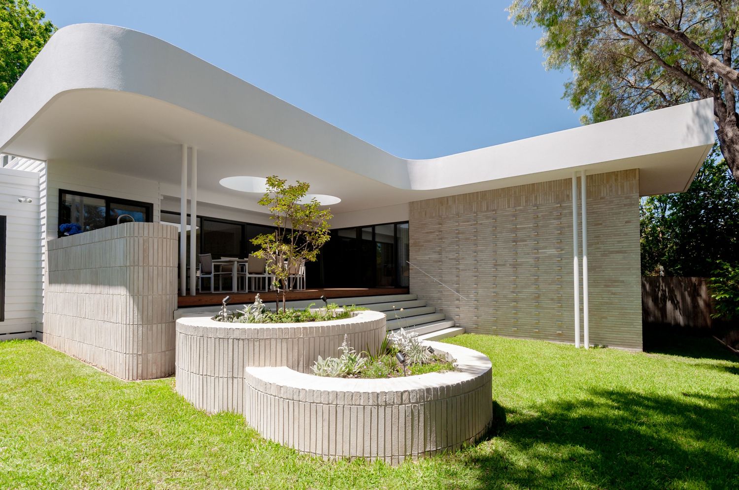 Contemporary white building with curved architecture and raised garden beds under blue sky.