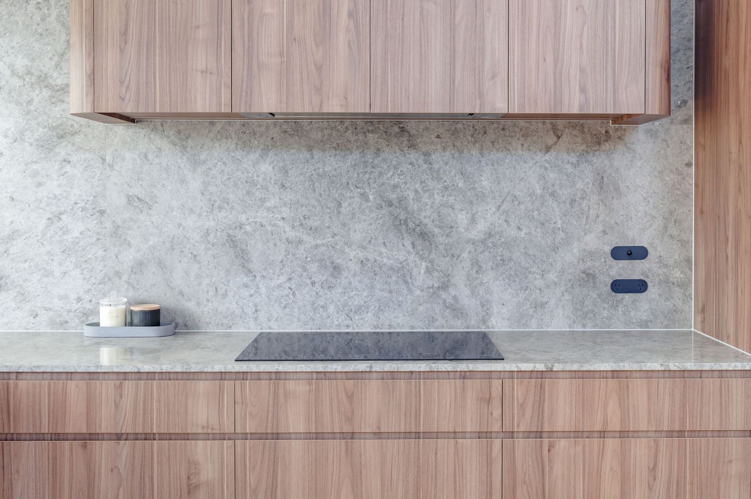 Sleek induction cooktop integrated into marble countertop with wooden cabinetry.