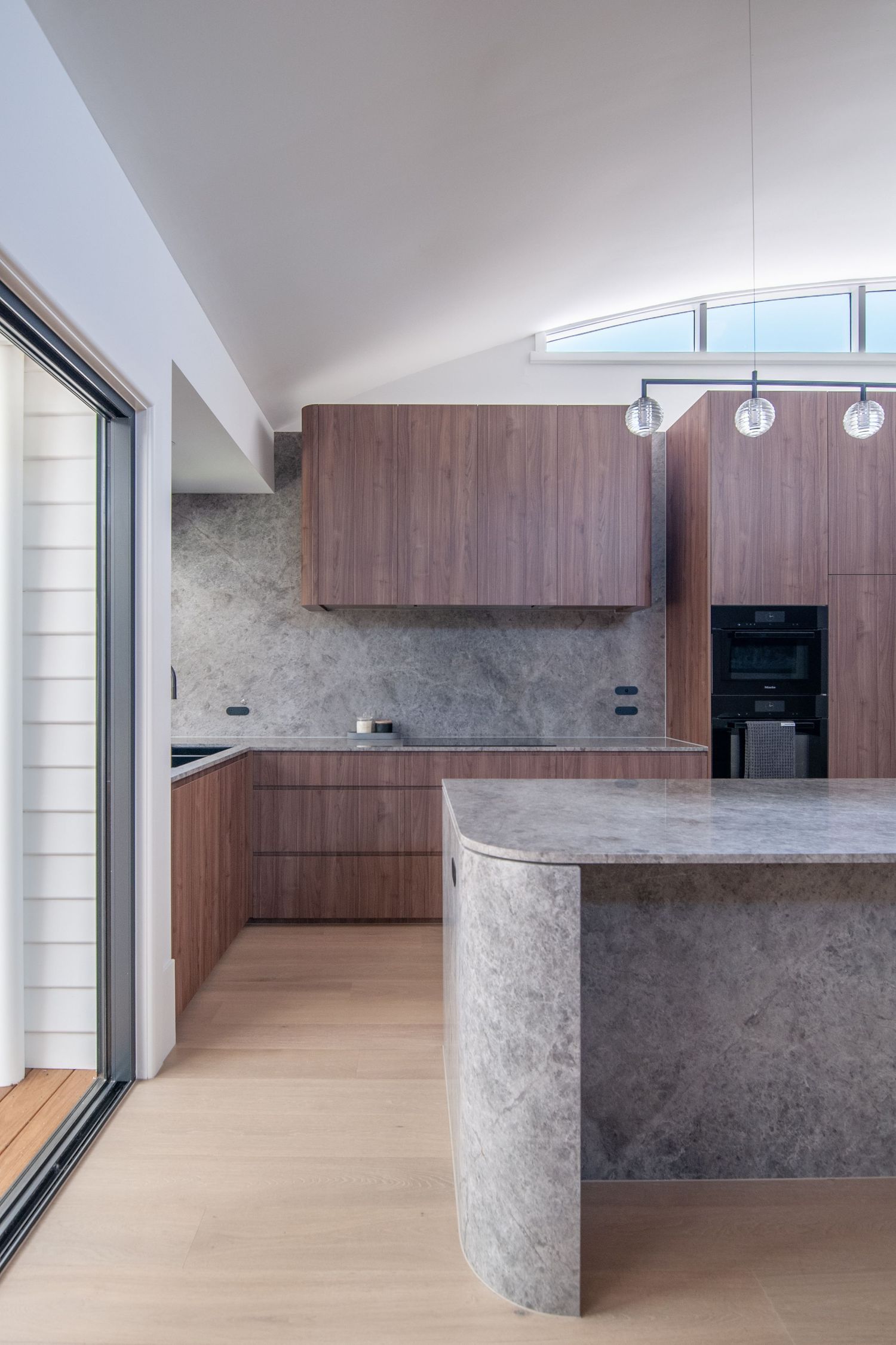 Contemporary kitchen with vaulted ceiling, pendant lights, and concrete island design.
