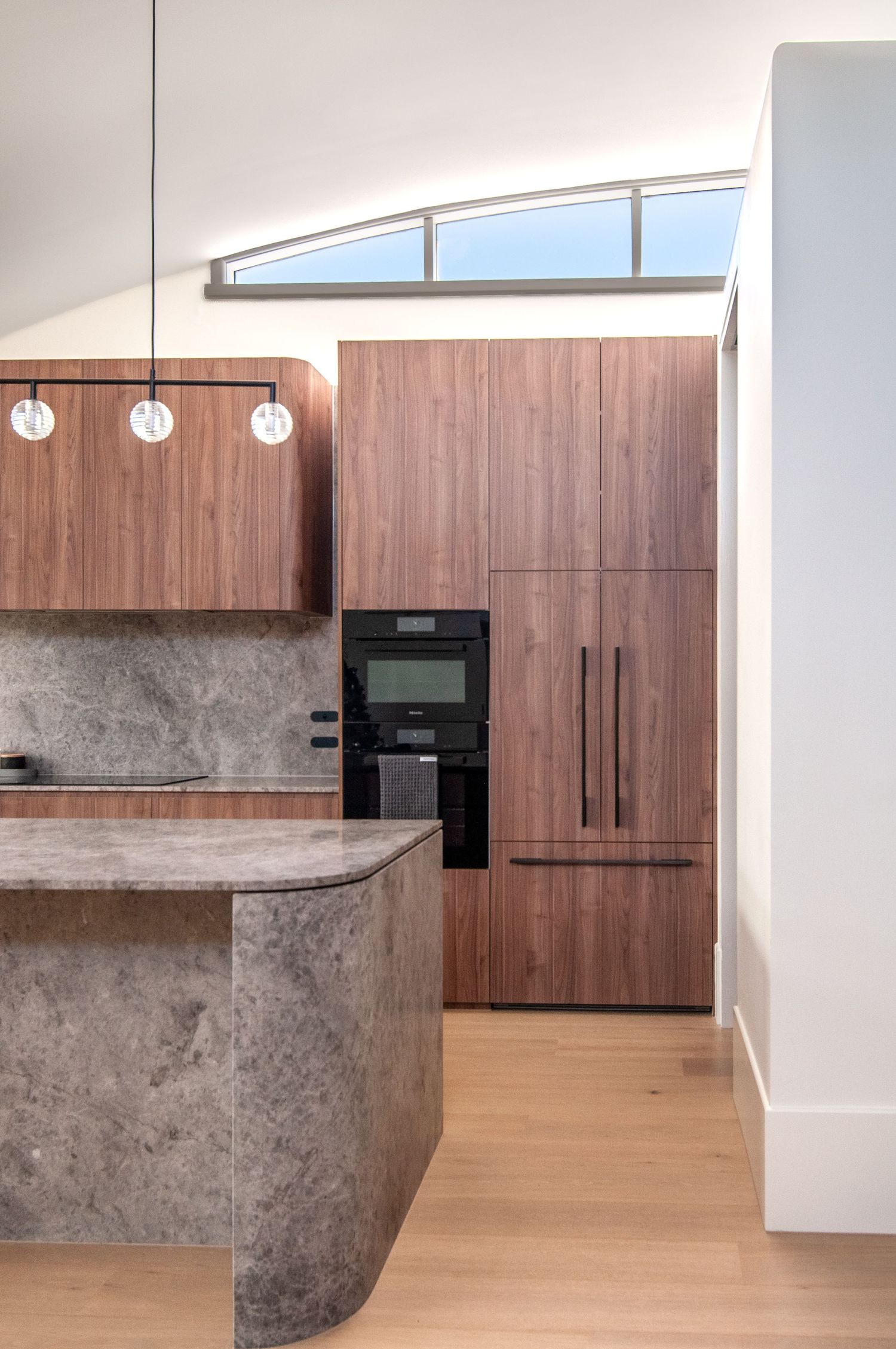Modern kitchen featuring angled ceiling windows, wood cabinetry, and concrete island.