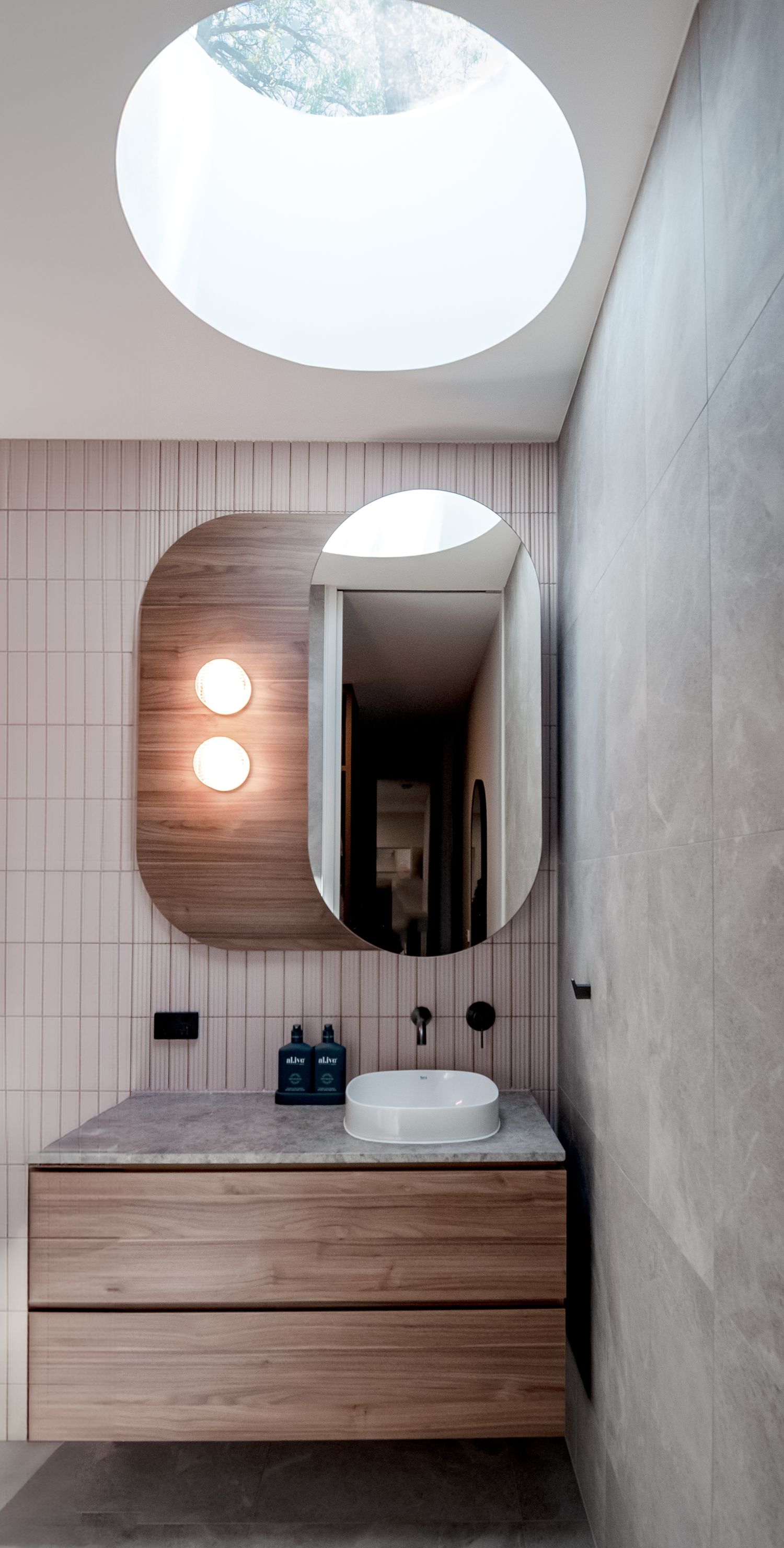 Modern bathroom featuring a floating wood vanity, oval mirror, and dramatic circular skylight.