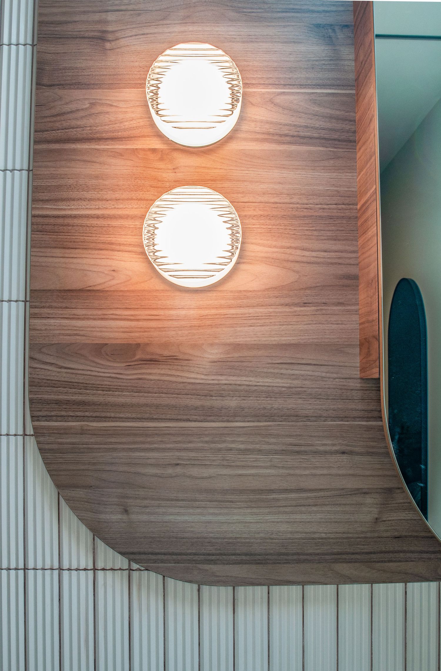 Wood-paneled curved wall with two illuminated circular sconces creating warm ambient lighting.