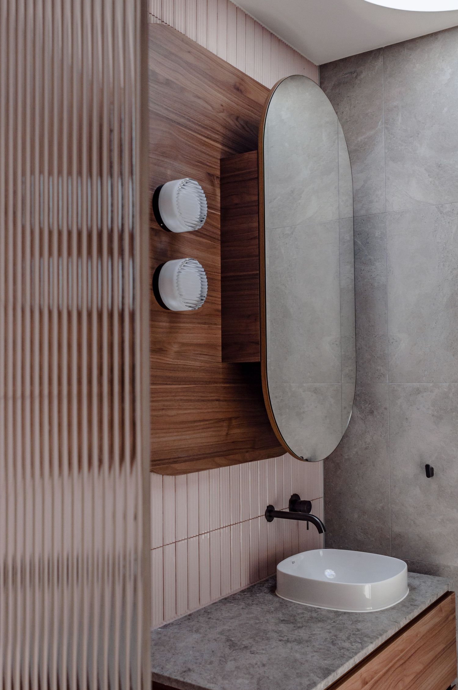 Contemporary bathroom design with oval mirror, round sconces, and mixed materials of wood and concrete.