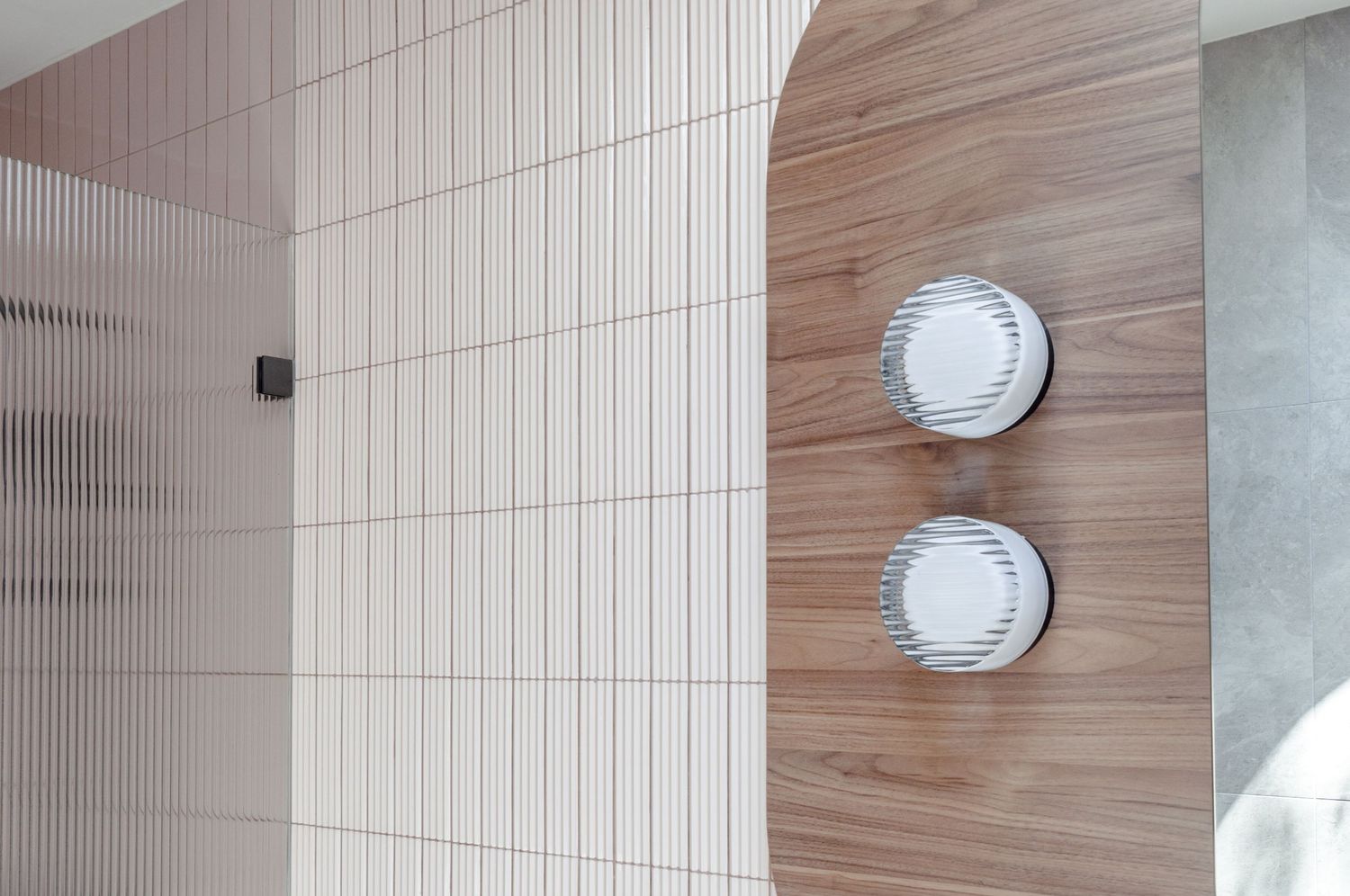 Minimalist bathroom detail showing round wall sconces mounted on wood and textured tile surfaces.