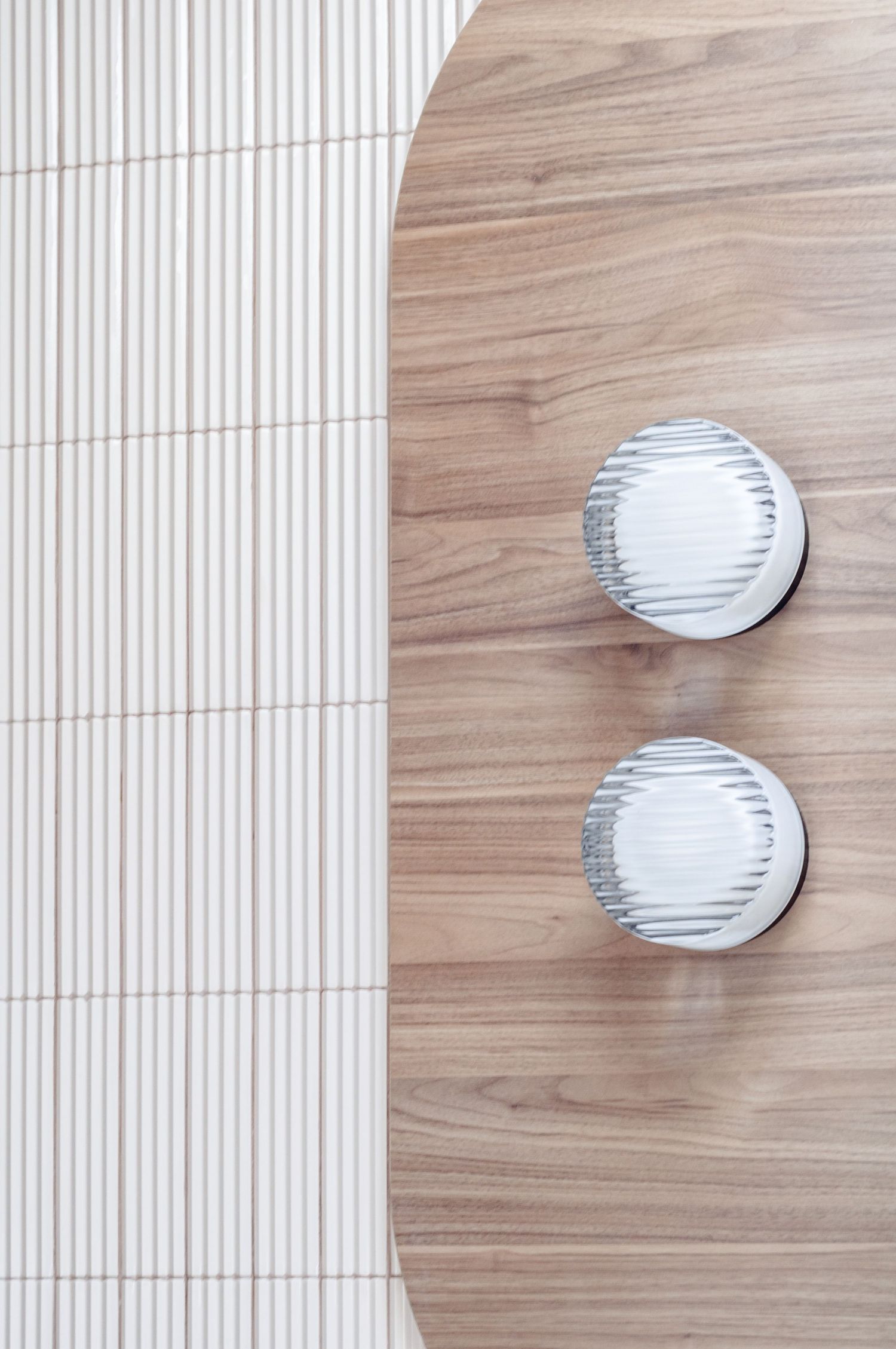 Close-up of two circular wall lights mounted on wood panel next to ribbed white tile.