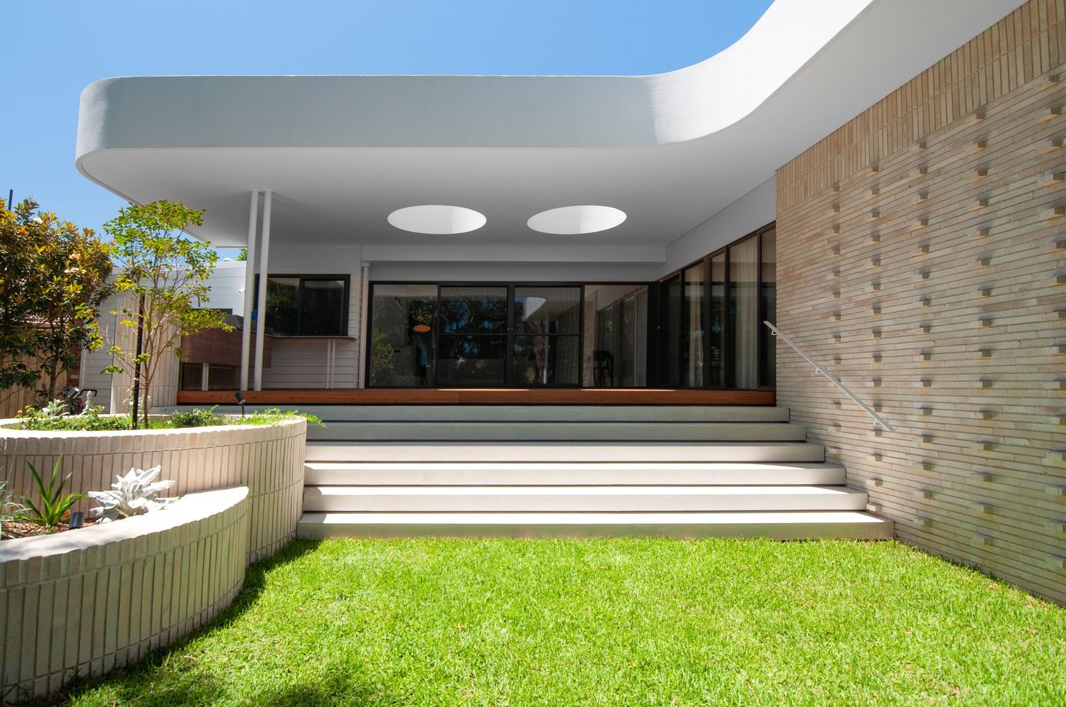 Minimalist architectural design with circular skylights and curved garden beds leading to entrance steps.