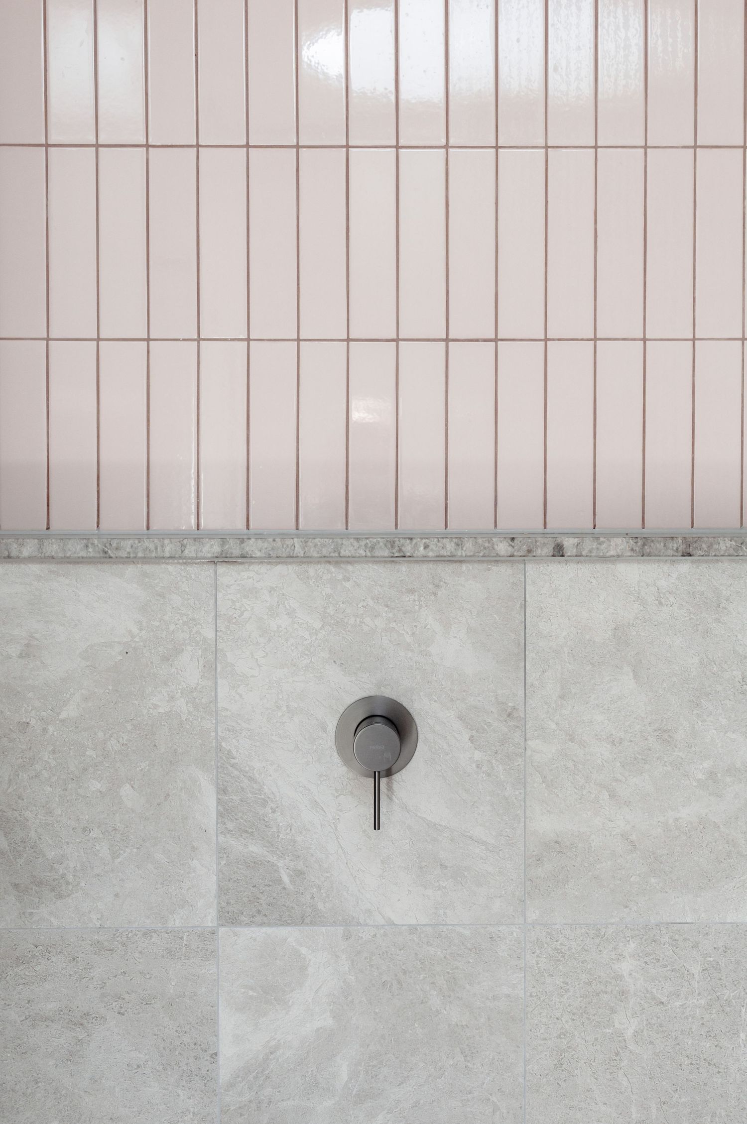 Modern bathroom wall with vertical beige tiles and a minimalist wall-mounted faucet.