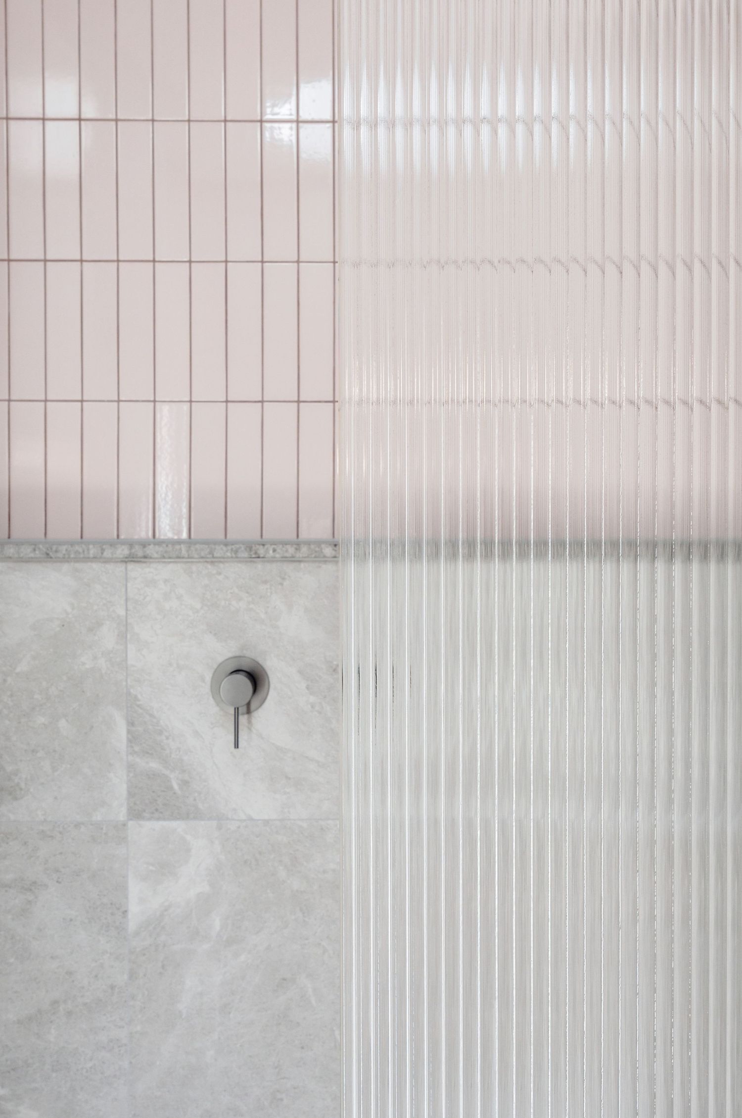 Close-up of modern bathroom wall featuring ribbed white tiles and concrete with minimalist fixtures.