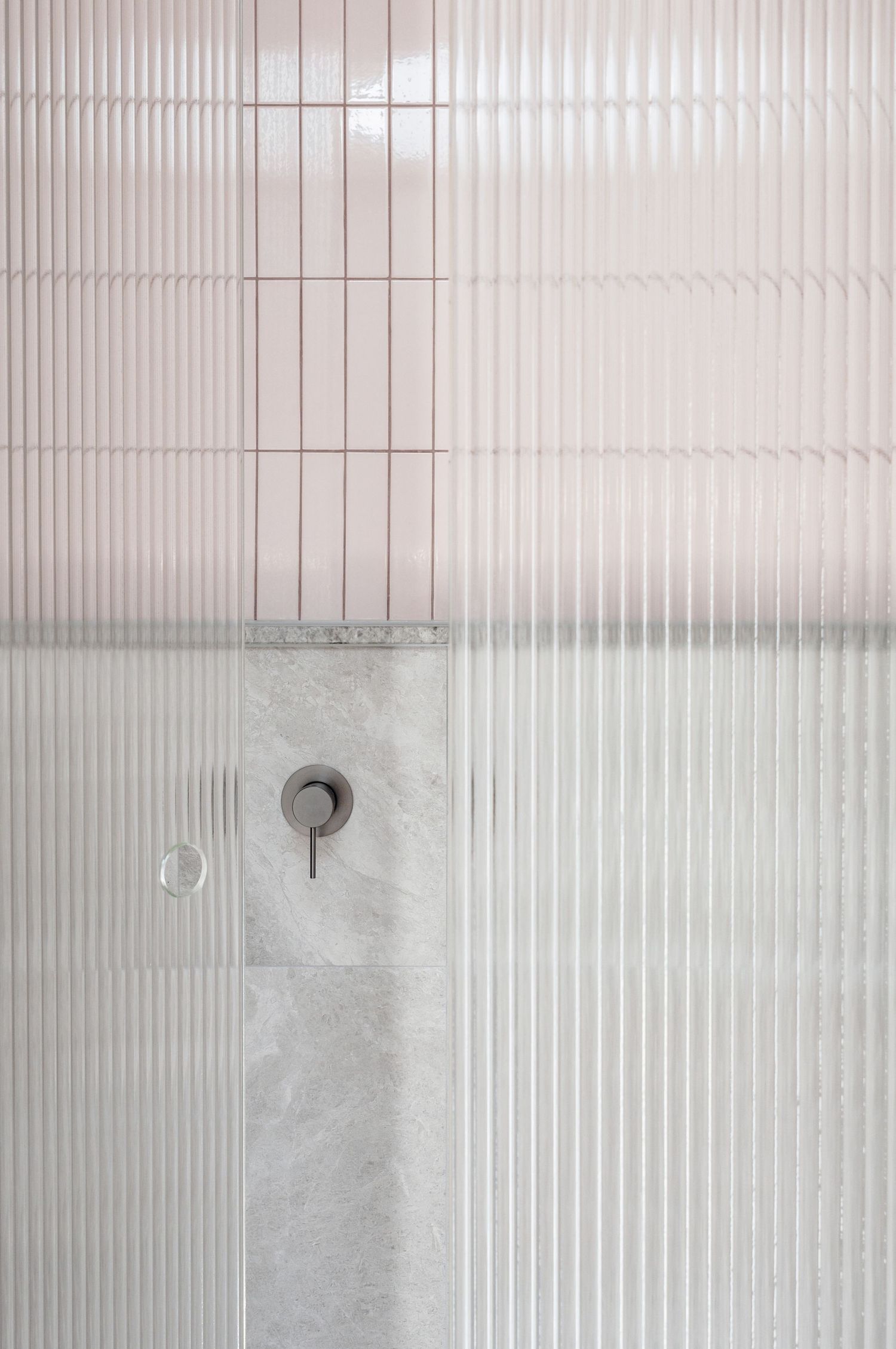 Minimalist bathroom wall detail showing textured white tiles and concrete with matte black fixtures.