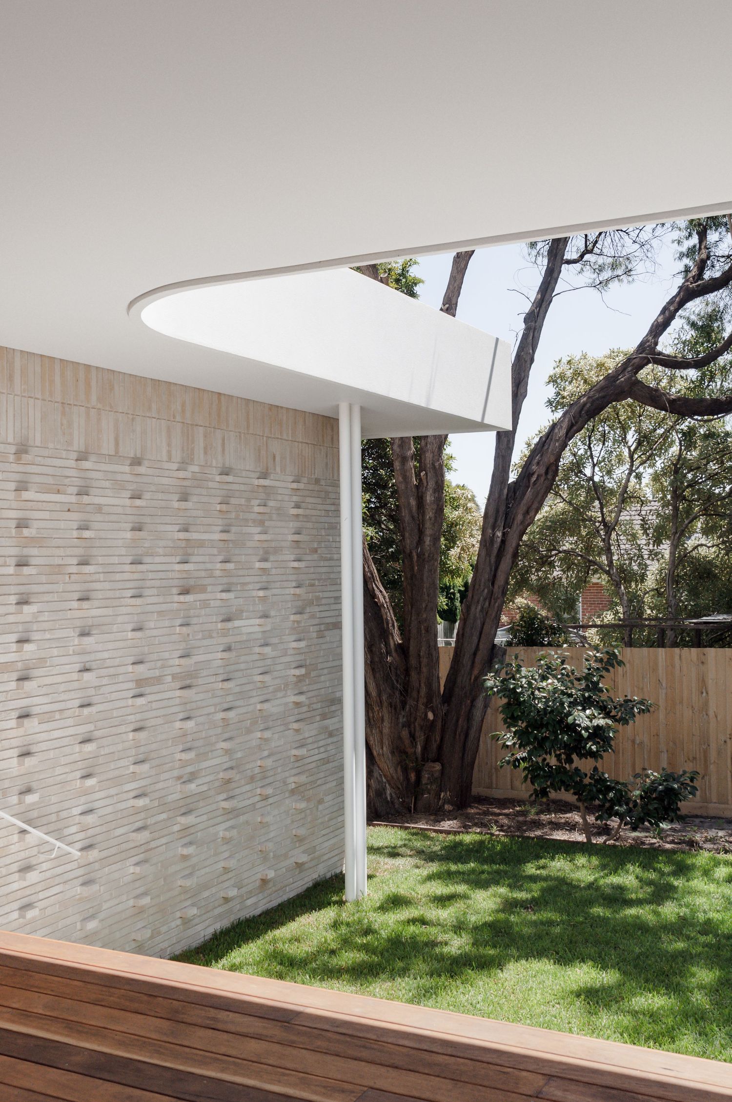 Contemporary outdoor space with textured brick wall, curved roof overhang, and landscaped garden.