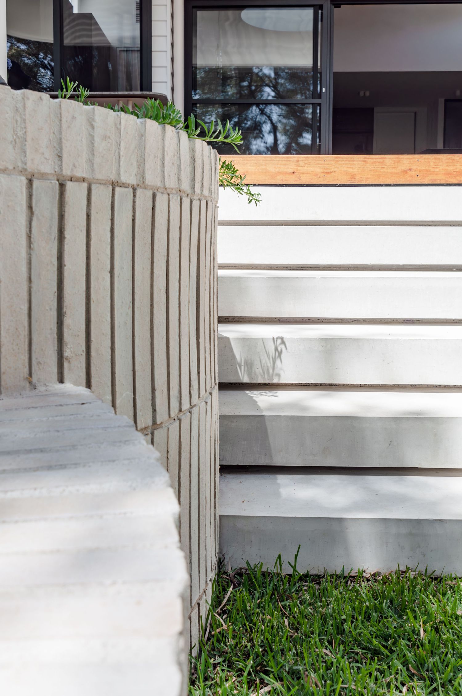 Curved concrete retaining wall with vertical lines leading to white steps and glass windows.
